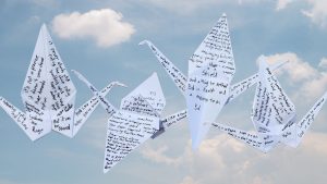 A photo of an origami crane with poetry written across its wings against the background of the sky.